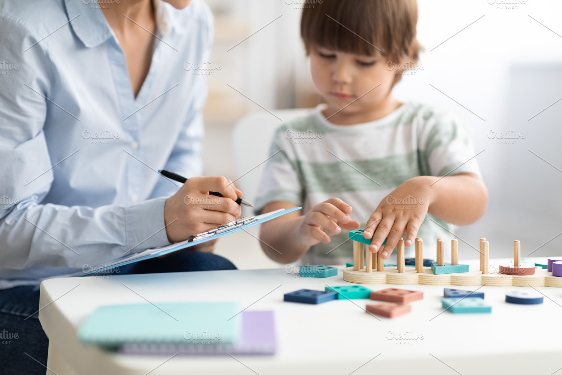 Little boy playing logical wooden toy at psychologist office, woman specialist, a Photo by Prostock-Studio