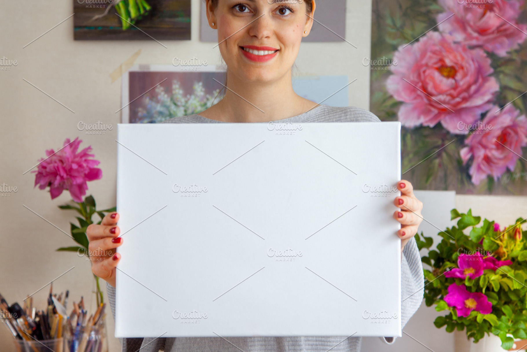Smiling young woman artist is holding a blank white canvas, a Holiday Photo by Natalia Kostikova