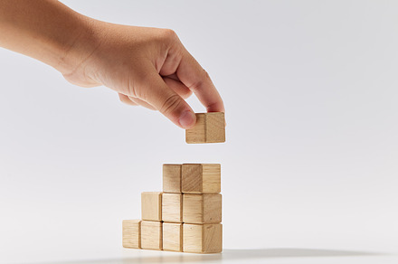 Hand putting wood cubes stacked as stair step shapes on white, a Business Photo by 1981 Rustic studio kan