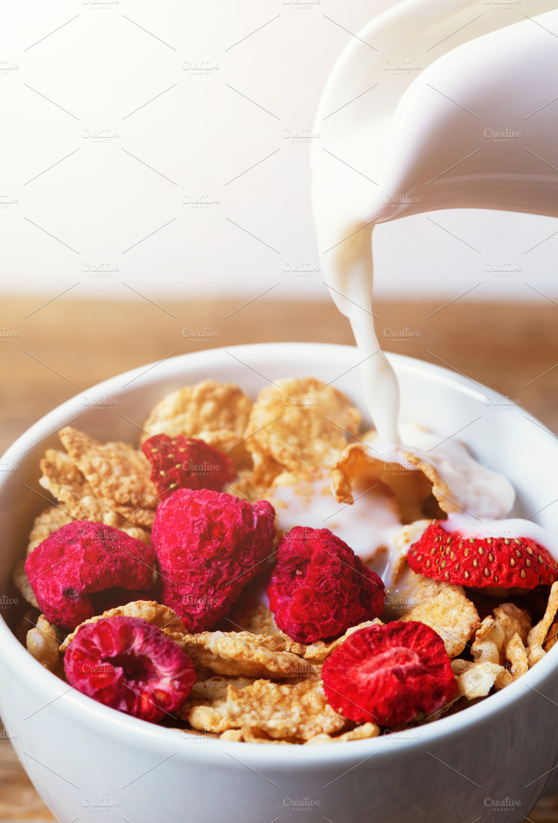 Pouring milk into bowl of cereal with raspberries and strawberries for breakfas, a Food & Drink Photo by Antonio Gravante Market