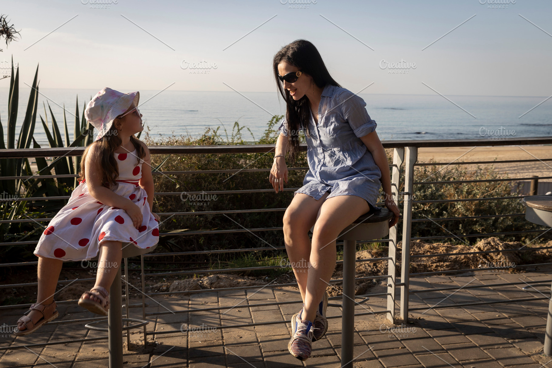 Mother and daughter sitting on tall stools near the beach, talki, a Person Photo by Imaginarium