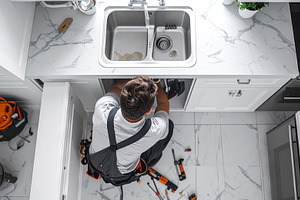 Plumber Repairing Sink in Modern Kit, an Industrial Photo by Stock Shape