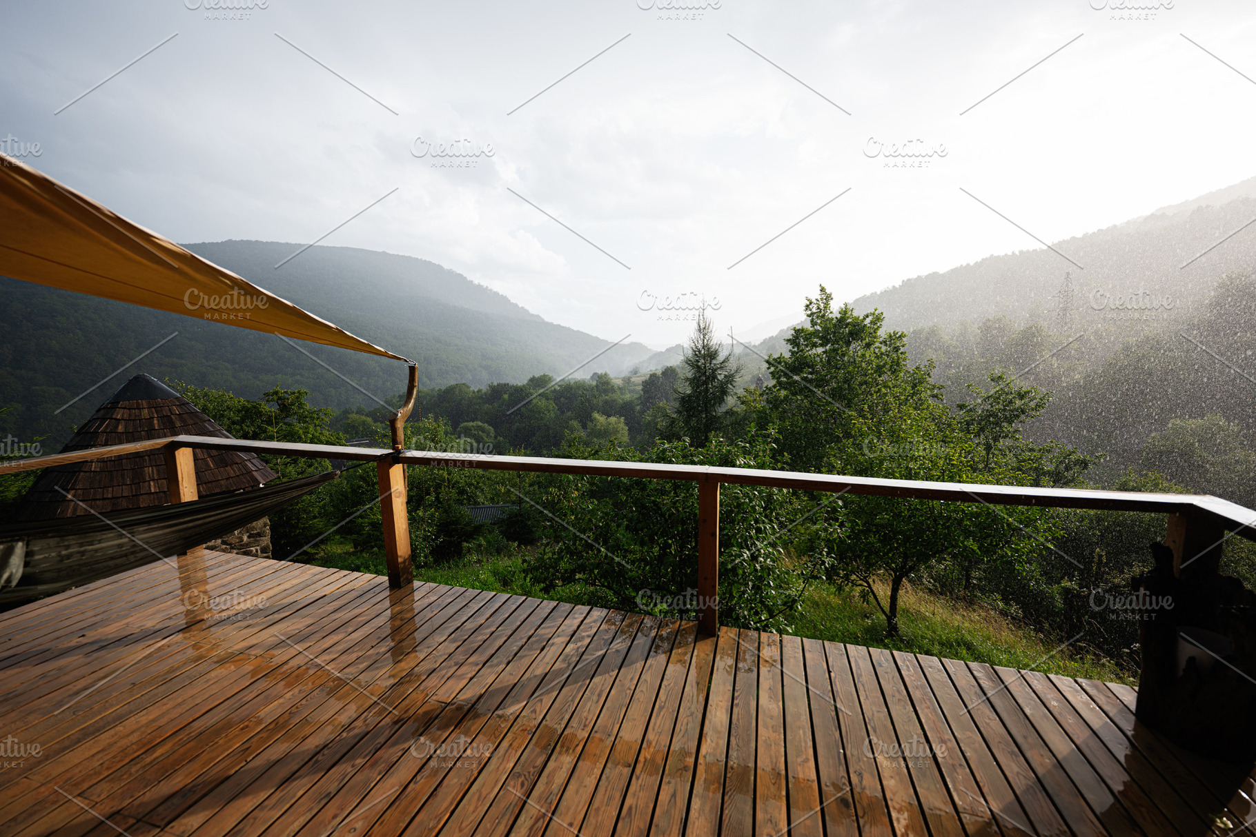 Wooden deck overlooking lush misty green valley under gentle rainfall, a Photo by AS photostudio