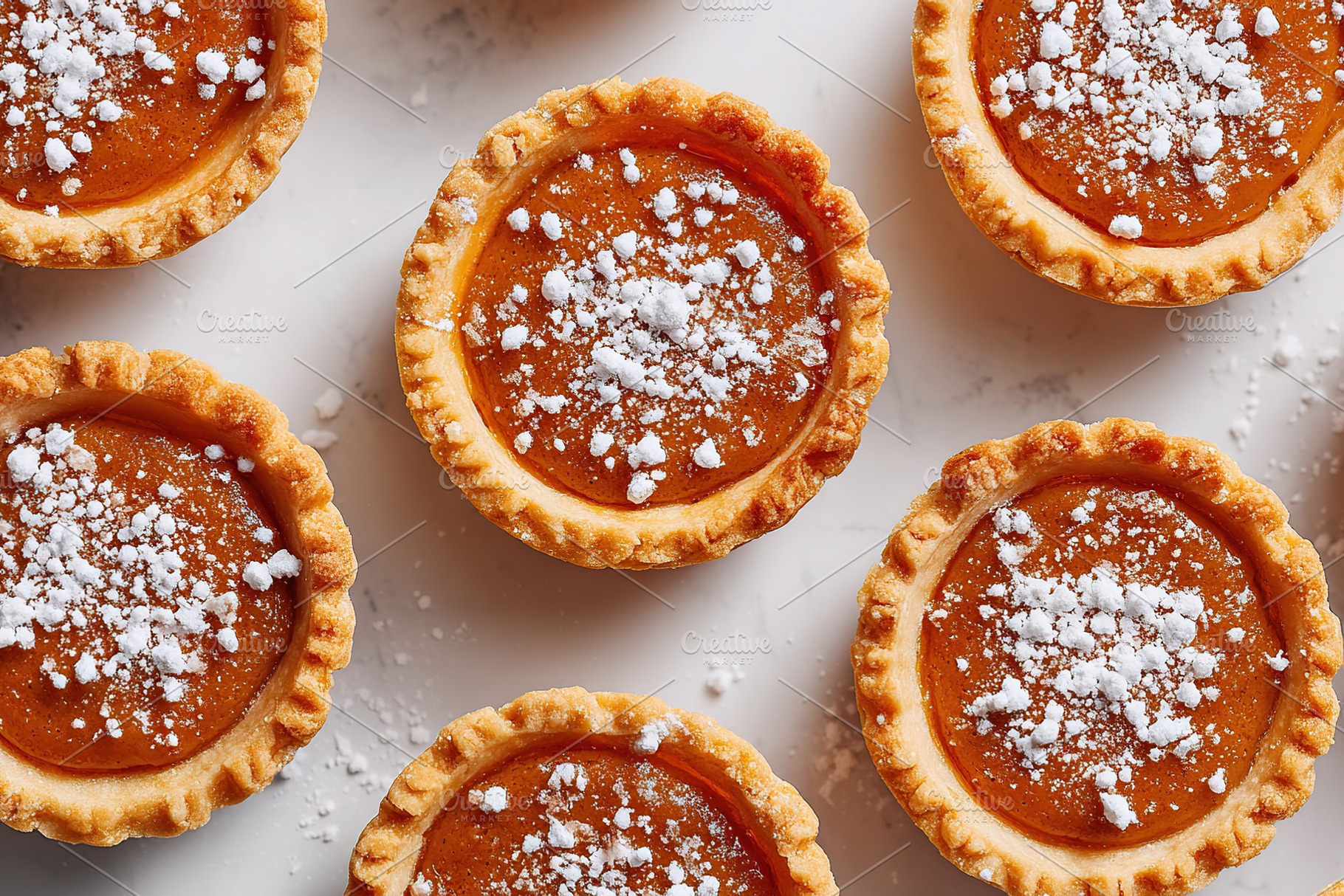 Pumpkin pie tarts on a white surface with powdered sugar sprinkles during autum, a Photo by AlyaAnd