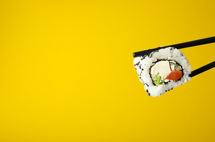 Chopsticks with sushi roll on yellow background, space for text., a Food & Drink Photo by AtlasStudio