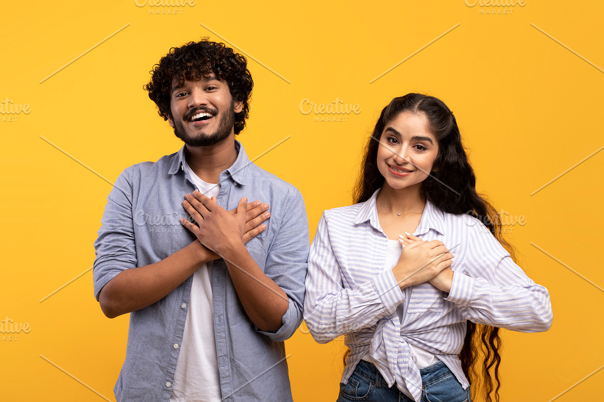 Thankful indian couple keeping both palms on chest, smiling at camera, expressi, a Photo by Prostock-Studio (Photo 2 of 3)