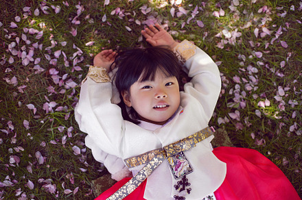 Korean girl child in a national costume lies on the back in a garden with cherr, a Person Photo by SaulichPhoto
