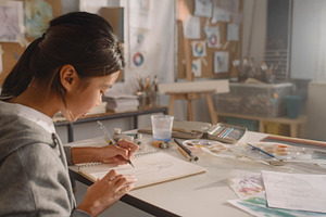 Asian teenager adding details to a sketchbook during an art clas, a School & Education Photo by DanFLCreativo