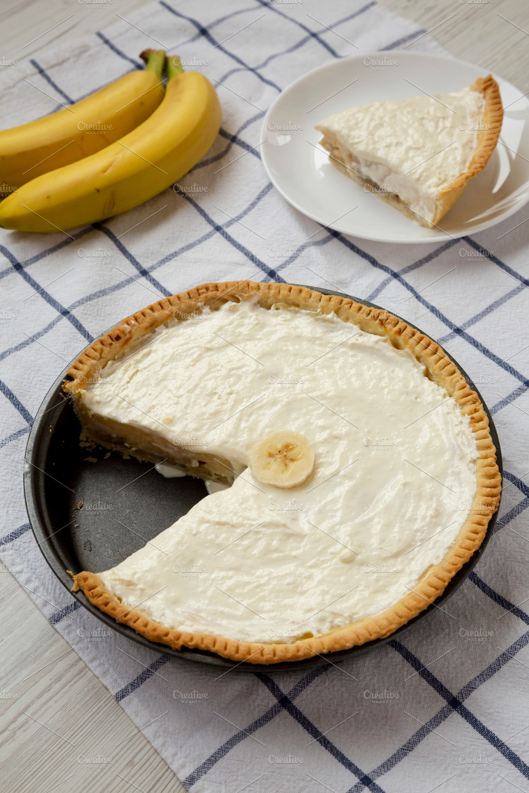 Homemade Tasty Banana Cream Pie on a white wooden table, low ang, a Food & Drink Photo by LiudmylaChuhunova