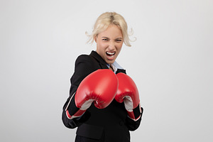 Angry young businesswoman in boxing gloves ready for fight over light grey back, a Photo by Prostock-Studio