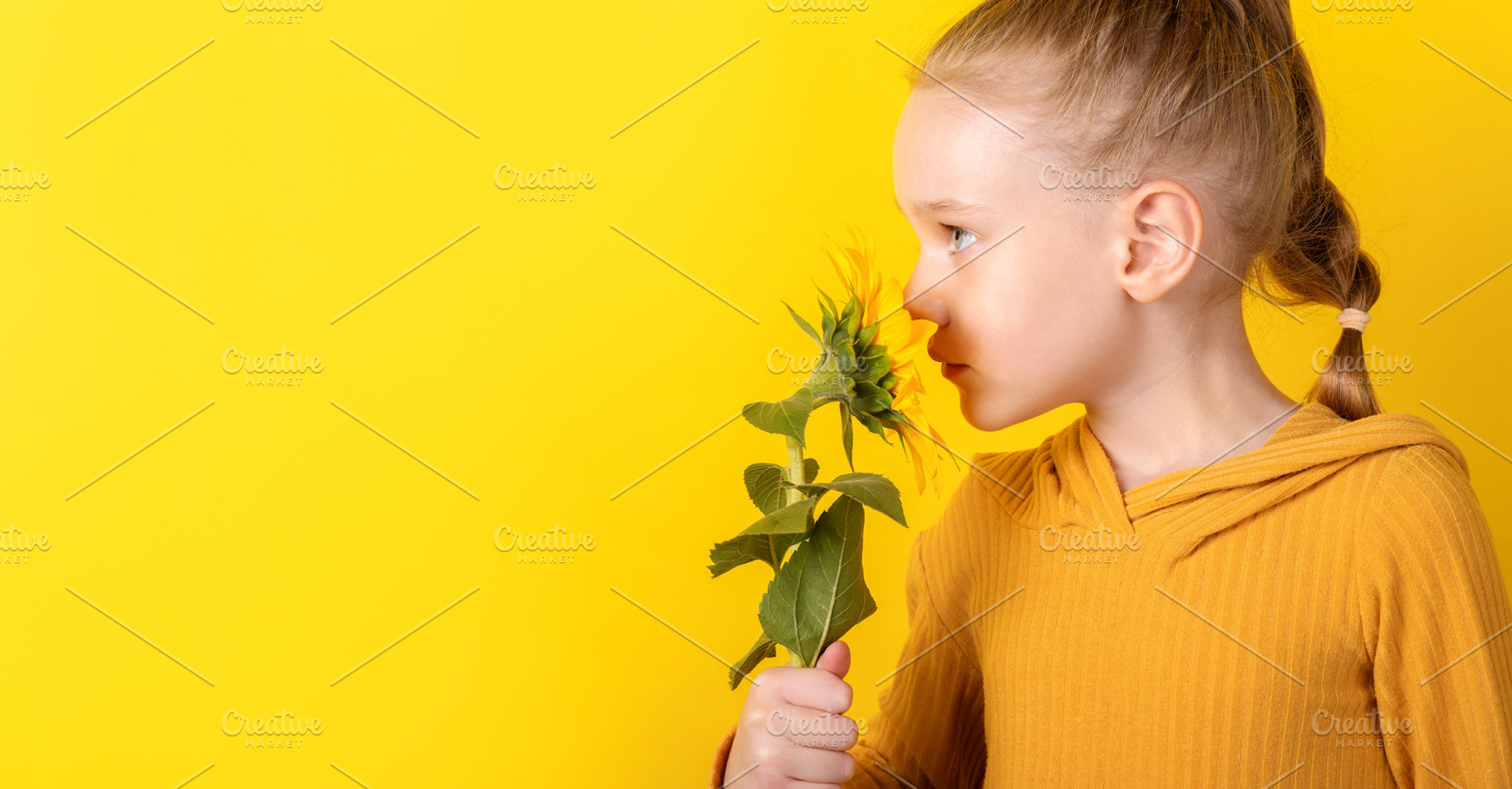 Young girl with blond hair holding and smelling a sunflower agai, a Person Photo by Ales Munt