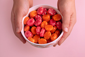 Bowl of vibrant orange and pink candies held in two hands on a p, a Food & Drink Photo by Ales Munt