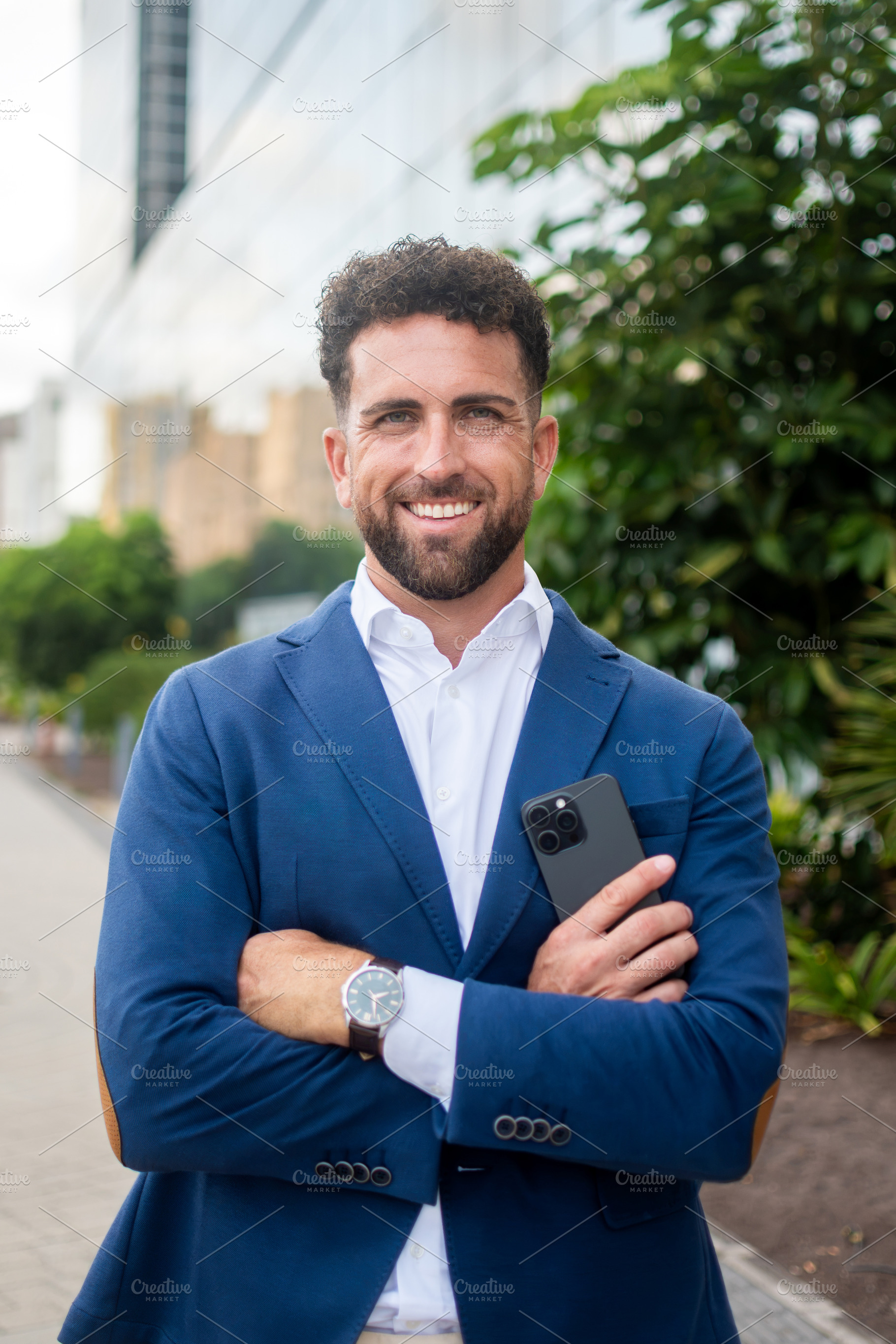 Confident businessman holding smartphone outside modern office building, a Business Photo by etorres69