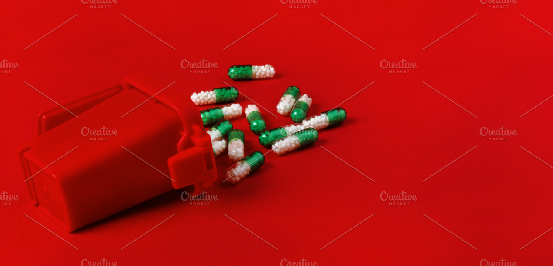 Green and white capsules scattered near a red medical container on bright red b, a Health & Medical Photo by Ales Munt