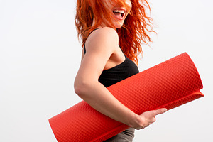 Cheerful sporty woman holding rolled up exercise mat against clear sky, a Photo by andreonegin market