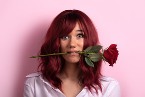 Young woman with red hair holds a single red rose in her mouth a, a Person Photo by Ales Munt