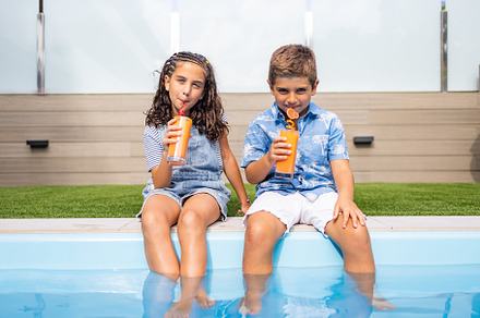 Two kids drinking orange juice in the swimming pool, a Person Photo by Cosca