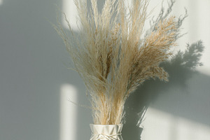 Home interior floral decor. Dried flowers in vase on white shelf. Background wi