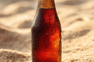 Cold soda bottle in sand, a Food & Drink Photo by Virgo Studio