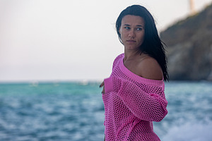 Young woman in a bright pink sweater standing by the ocean, gazing away, with a, a Person Photo by Ales Munt