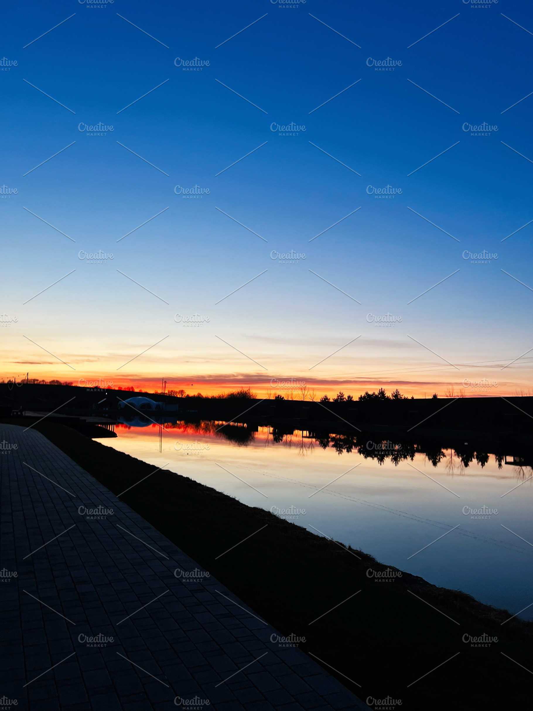 Serene sunset reflecting on a calm water canal with vibrant colors, a Photo by AS photostudio