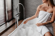 Young lady wrapped in towel preparing to take bath, sitting on bathtub and touc, a Photo by Prostock-Studio (Thumbnail 3 of 5)
