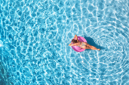 Aerial view of a young woman in hat swimming with pink swim ring, a Holiday Photo by den-belitsky