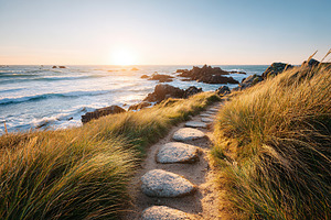 Walk along a quiet coastal path at sunset with golden light on the ocean, a Photo by AlyaAnd
