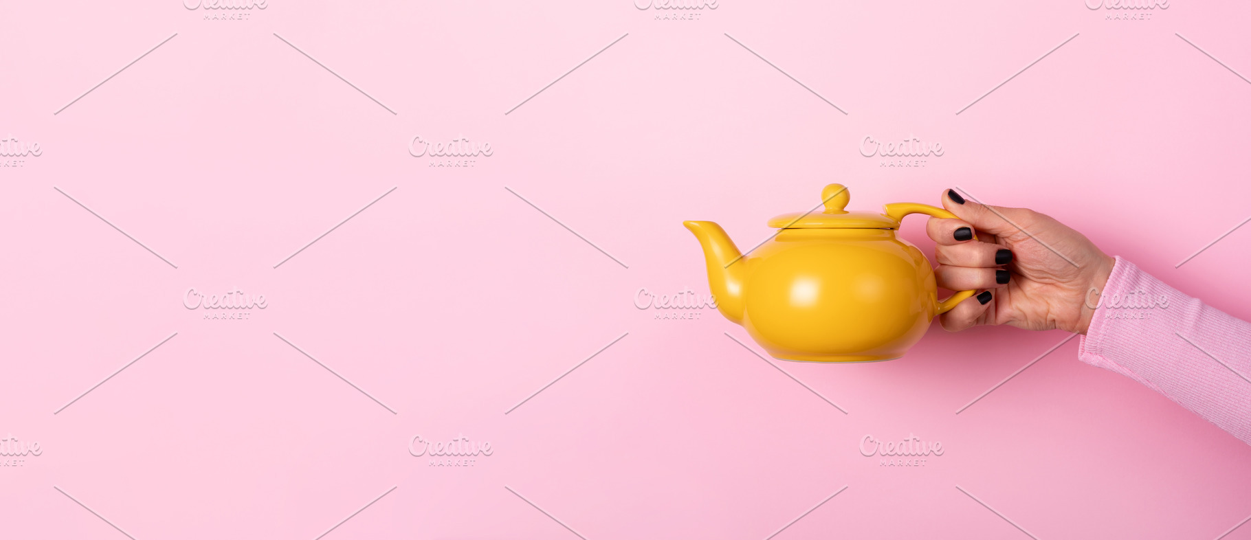 Female hand holding a yellow ceramic teapot against a pastel pin, a Food & Drink Photo by Ales Munt