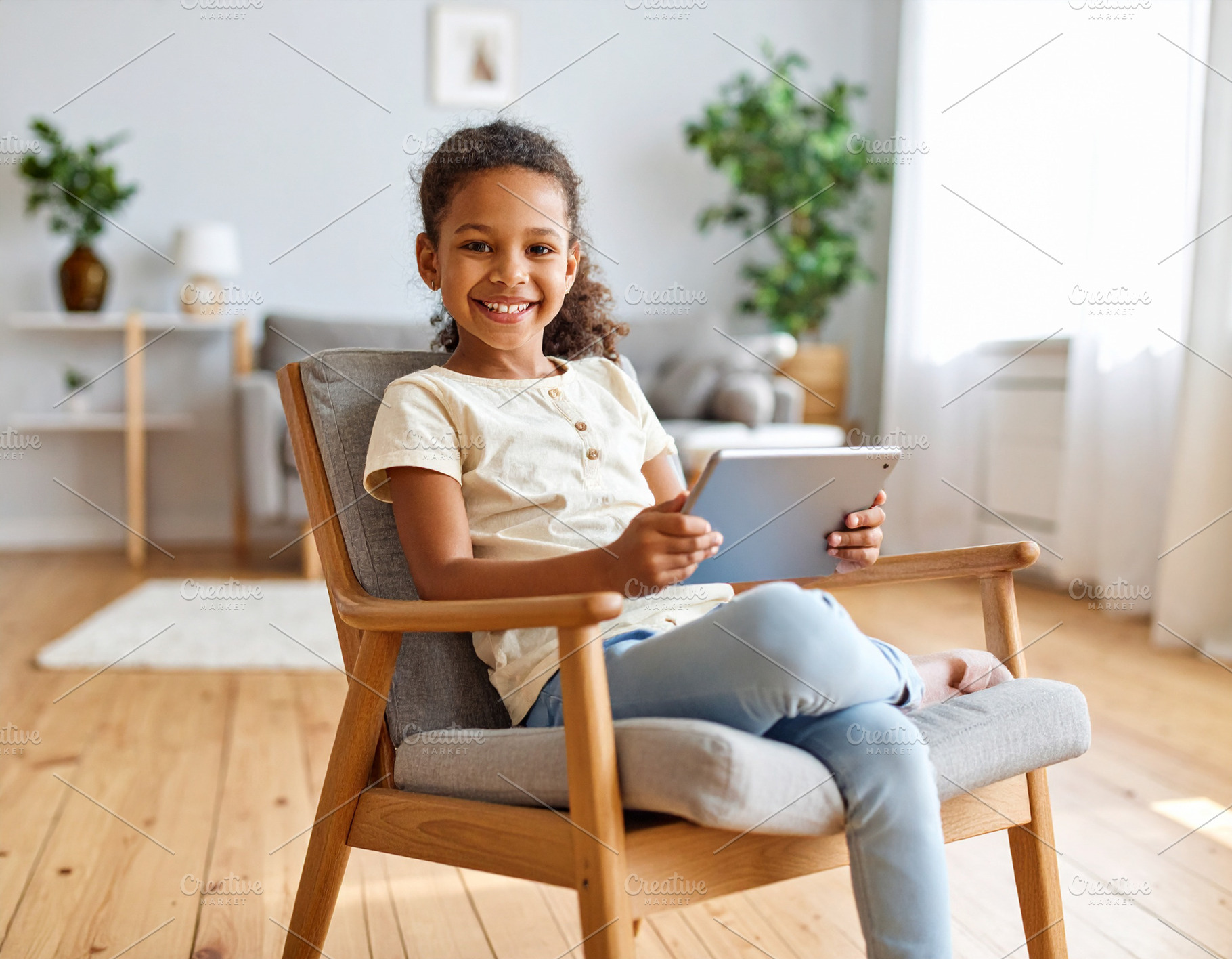 Girl with a tablet sitting on chair at living room while smiling, a Person Photo by DanFLCreativo