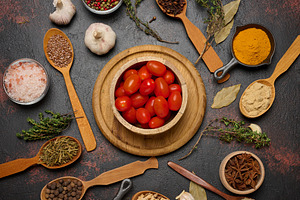 Cherry tomatoes in a wooden bowl and various spices on a dark ta, a Food & Drink Photo by ndanko