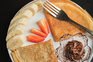 A plate of crepes filled with chocolate spread and topped with banana slices an