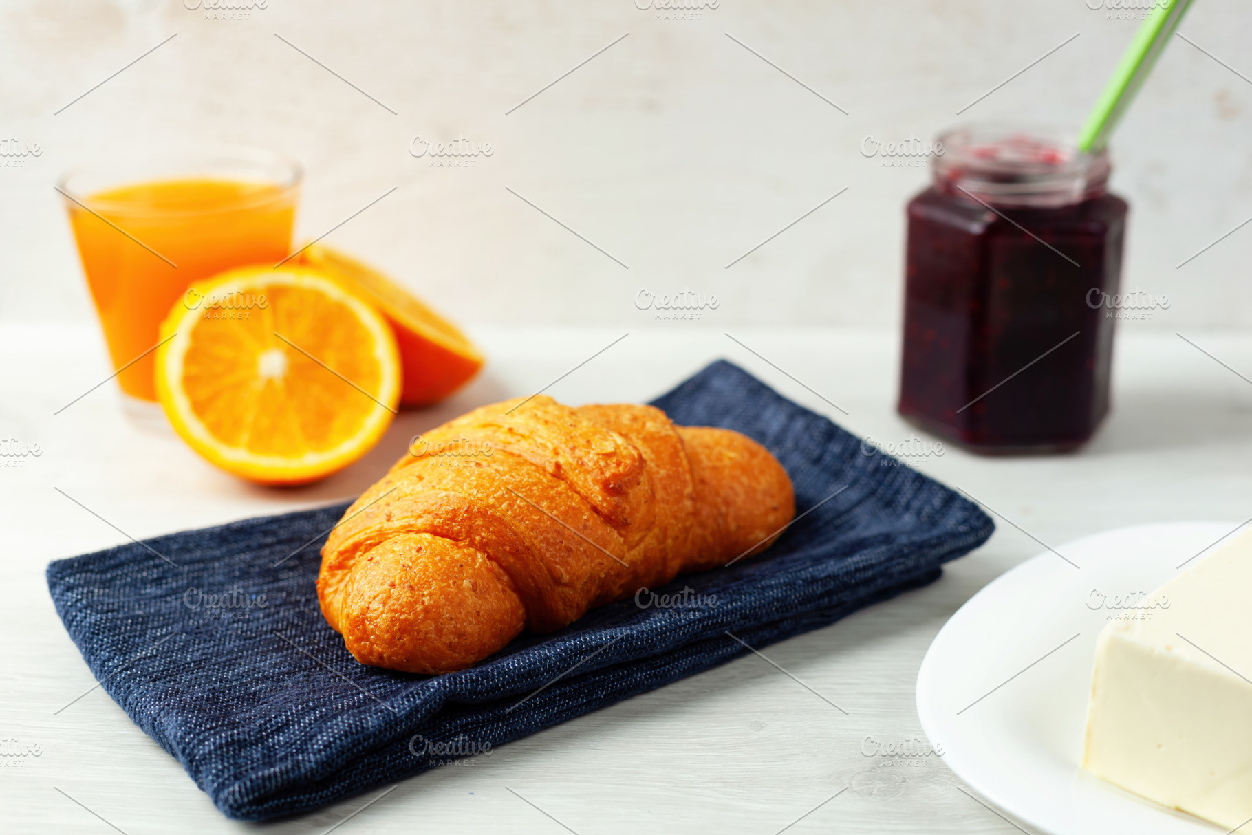 Delicious croissant resting on blue napkin with orange juice, jam and butter fo, a Food & Drink Photo by Antonio Gravante Market