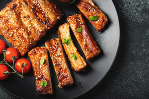 Hot grilled spare ribs from a summer BBQ served on a plate with sauce. Top view, a Food & Drink Photo by Budarinphoto