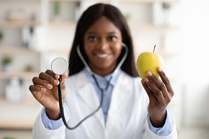 African american nutritionist showing organic green apple and using stethoscope, a Person Photo by Prostock-Studio