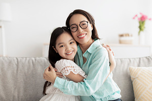 Happy little Asian girl and her loving grandmother hugging and looking at camer, a Photo by Prostock-Studio