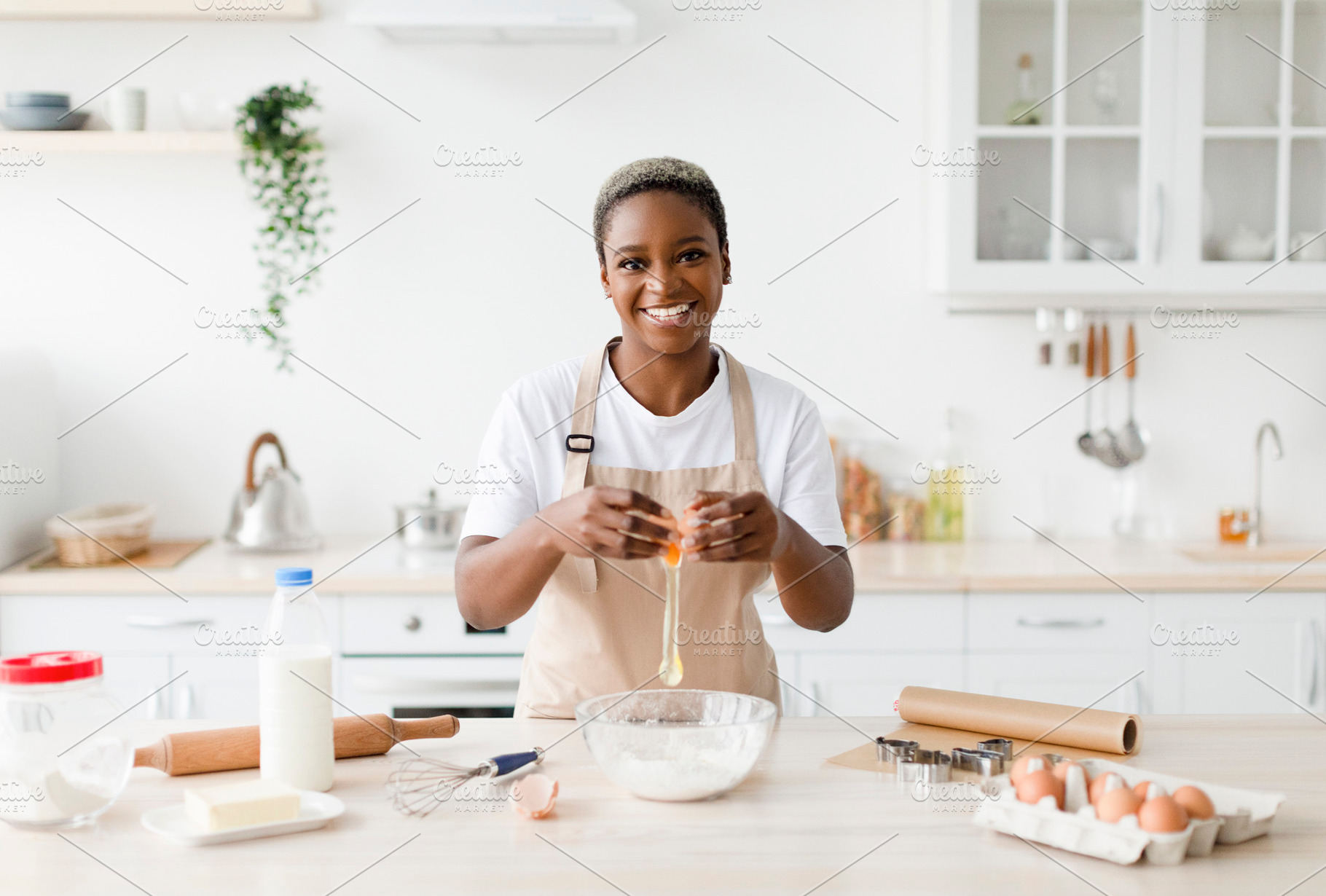 Cheerful young pretty black female in apron breaks egg, prepare baking pie or p, a Person Photo by Prostock-Studio