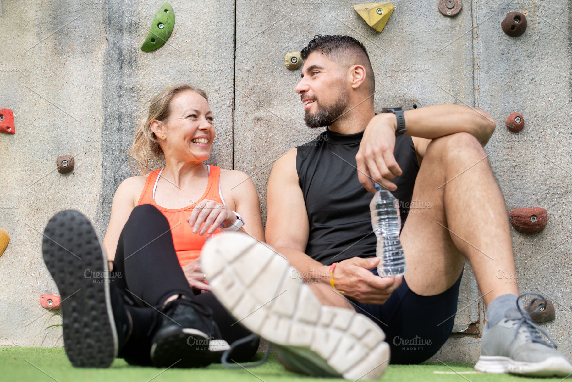 Active couple resting after workout and talking near climbing wall outdoors, a Food & Drink Photo by etorres69