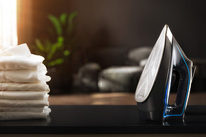 Iron on black living room table with white shirts stacked, a Technology Photo by Davizro's Market