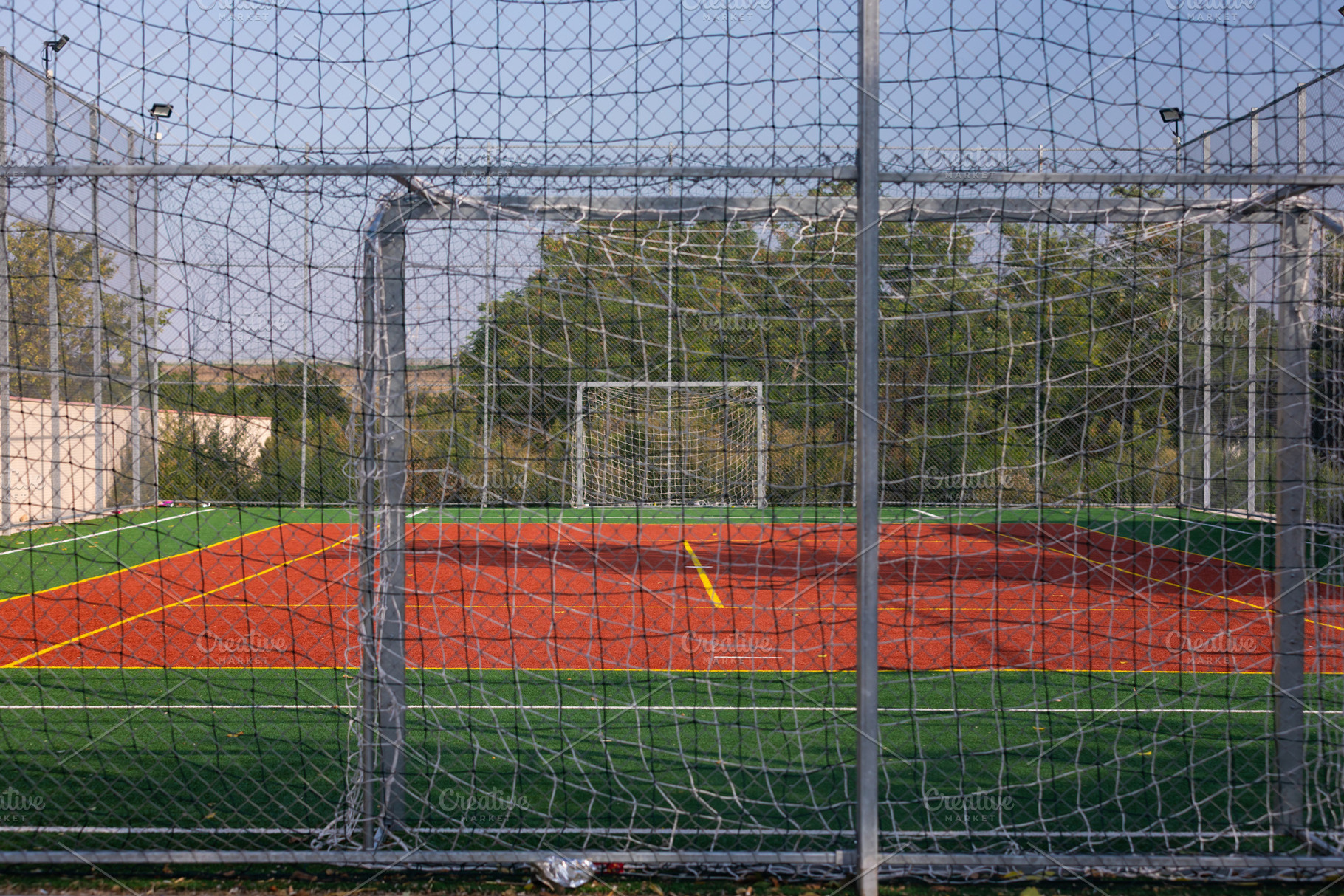 Wide shot of an empty soccer field with red turf, green borders, and netted goa, a Sports & Recreation Photo by Ales Munt