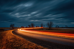 Night road curving light trails unde, a Photo by Pixeness Studio