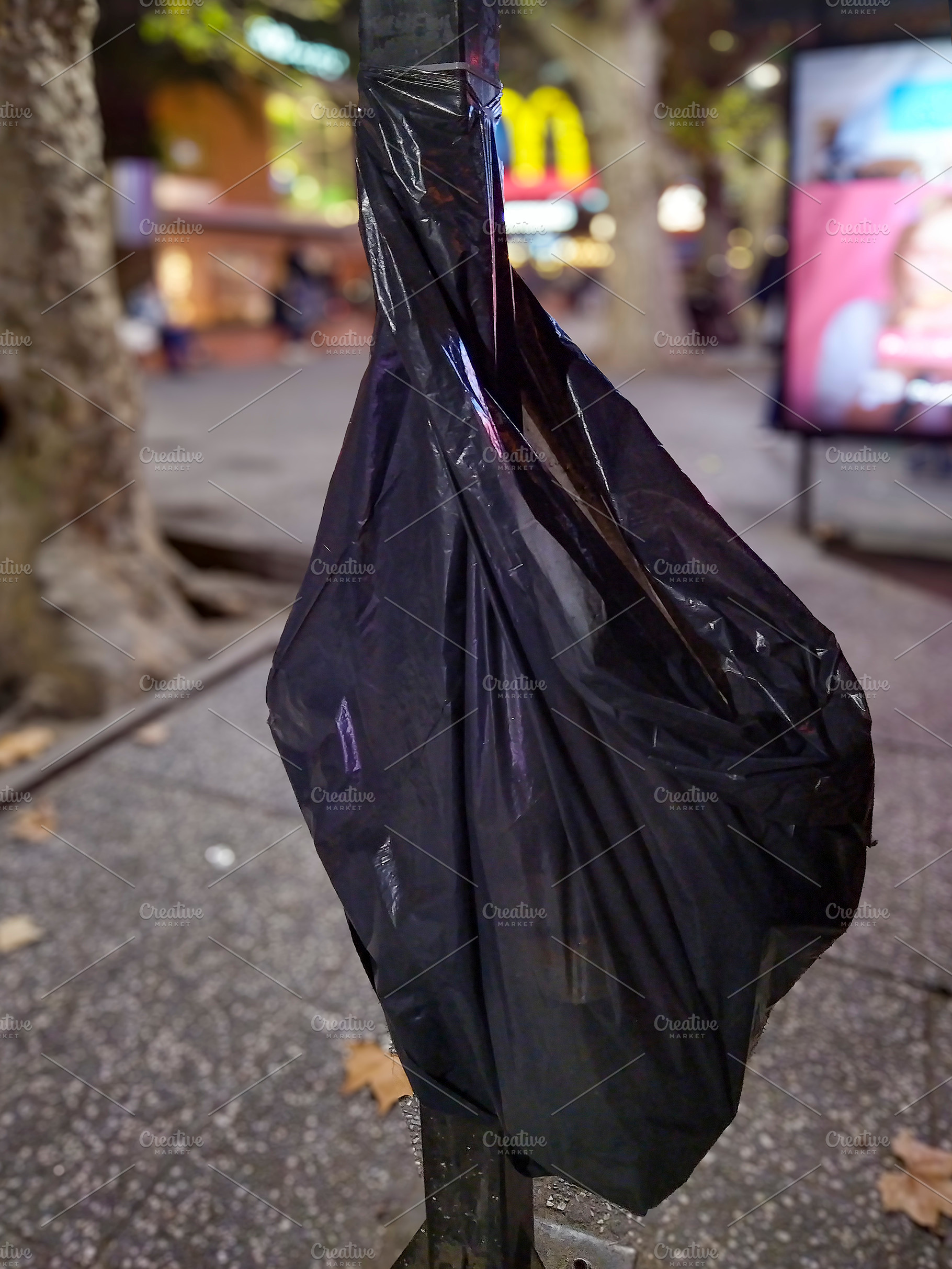 Black trash bag hanging on tree in city at night, a Background Photo by DanFLCreativo