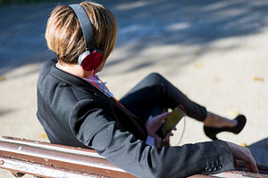Businesswoman listening to music on park bench, a Photo by RF Images