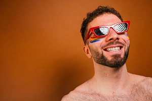 Smiling man celebrating pride with rainbow face paint, a Photo by karrastock