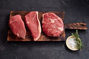 Raw rib-eye, roast beef, flank and rump steak on a wooden board with salt and h, a Food & Drink Photo by Asya Nurullina