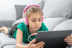 Young girl wearing headphones using tablet while relaxing on sofa at home, a Person Photo by etorres69