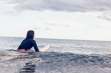 Rear view of a woman sitting on surfboard in water, a Photo by wavebreak