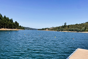 Scenic lake view with hills and dock in central Portugal under clear blue skies, a Photo by AS photostudio