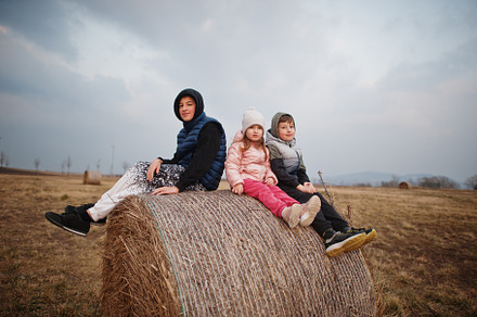 Three kids sitting on haycock at field., a Person Photo by AS photostudio