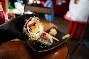 Close-up of gourmet sushi roll held with gloved hand in a cozy restaurant, a Photo by AS photostudio